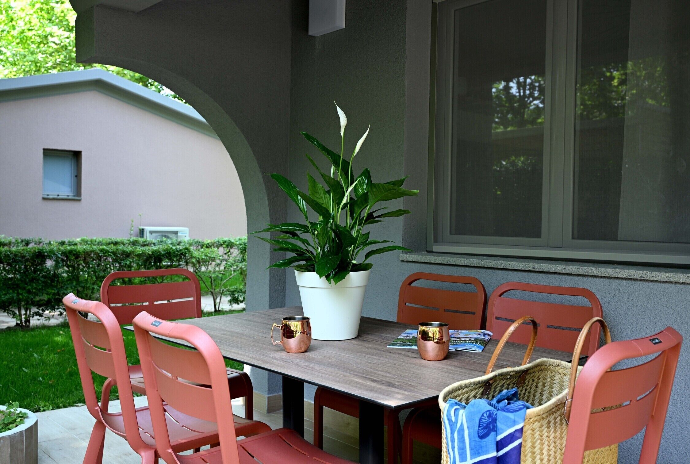 An outdoor patio with a table, chairs, a potted plant, and a basket.