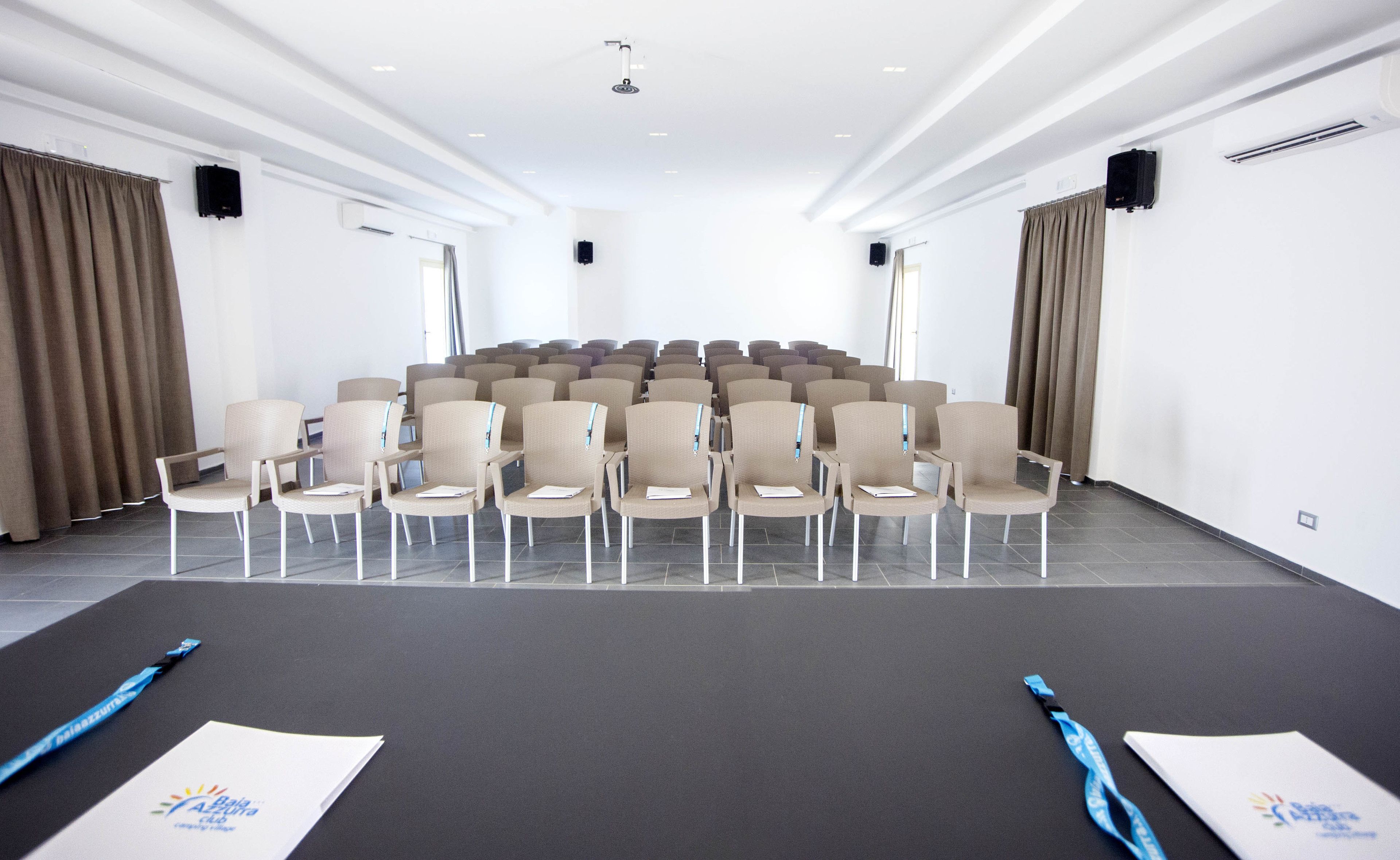 A conference room with rows of beige chairs, a black carpet, and a white ceiling.