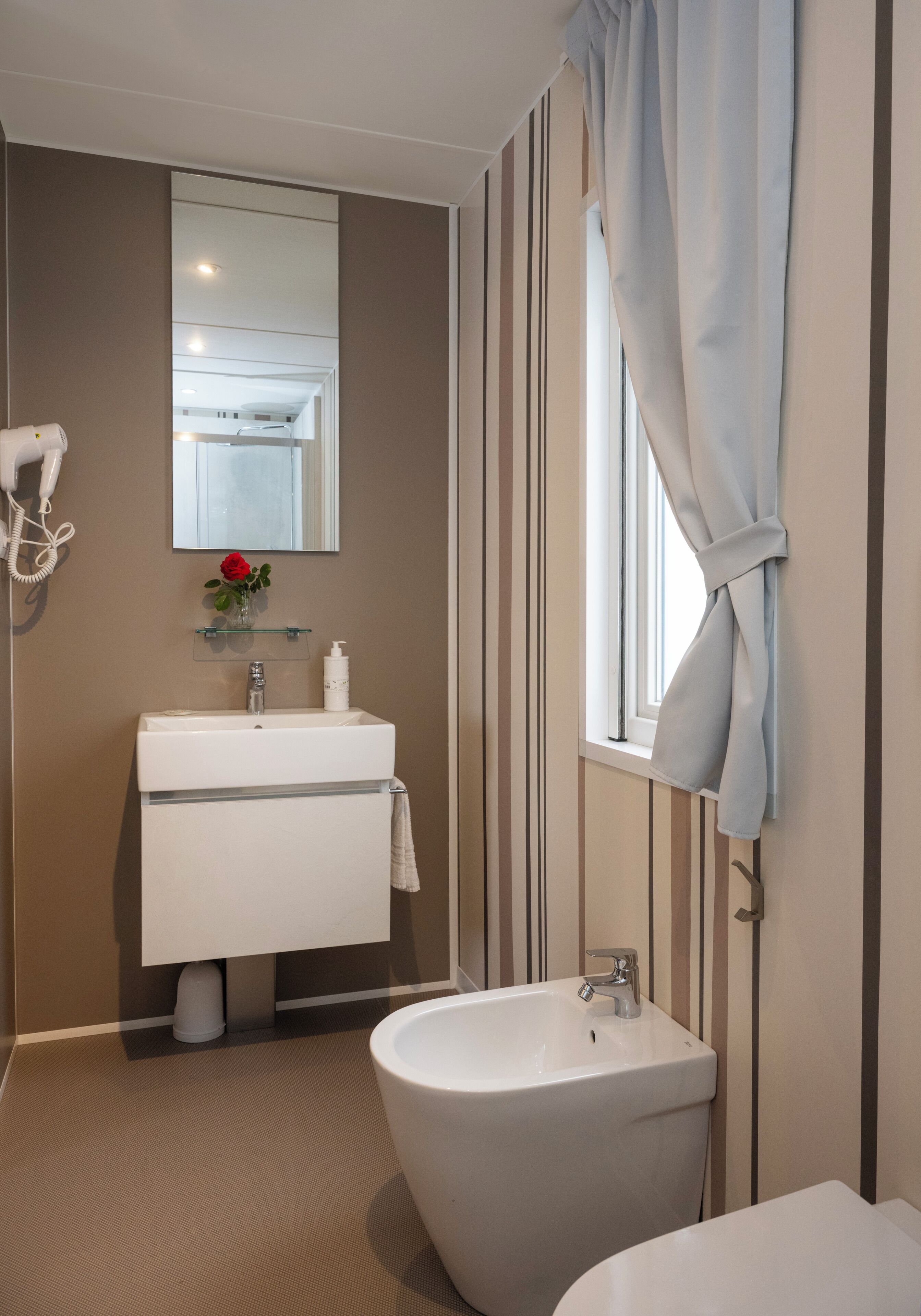 Un baño con lavamanos, espejo y ventana con cortinas.