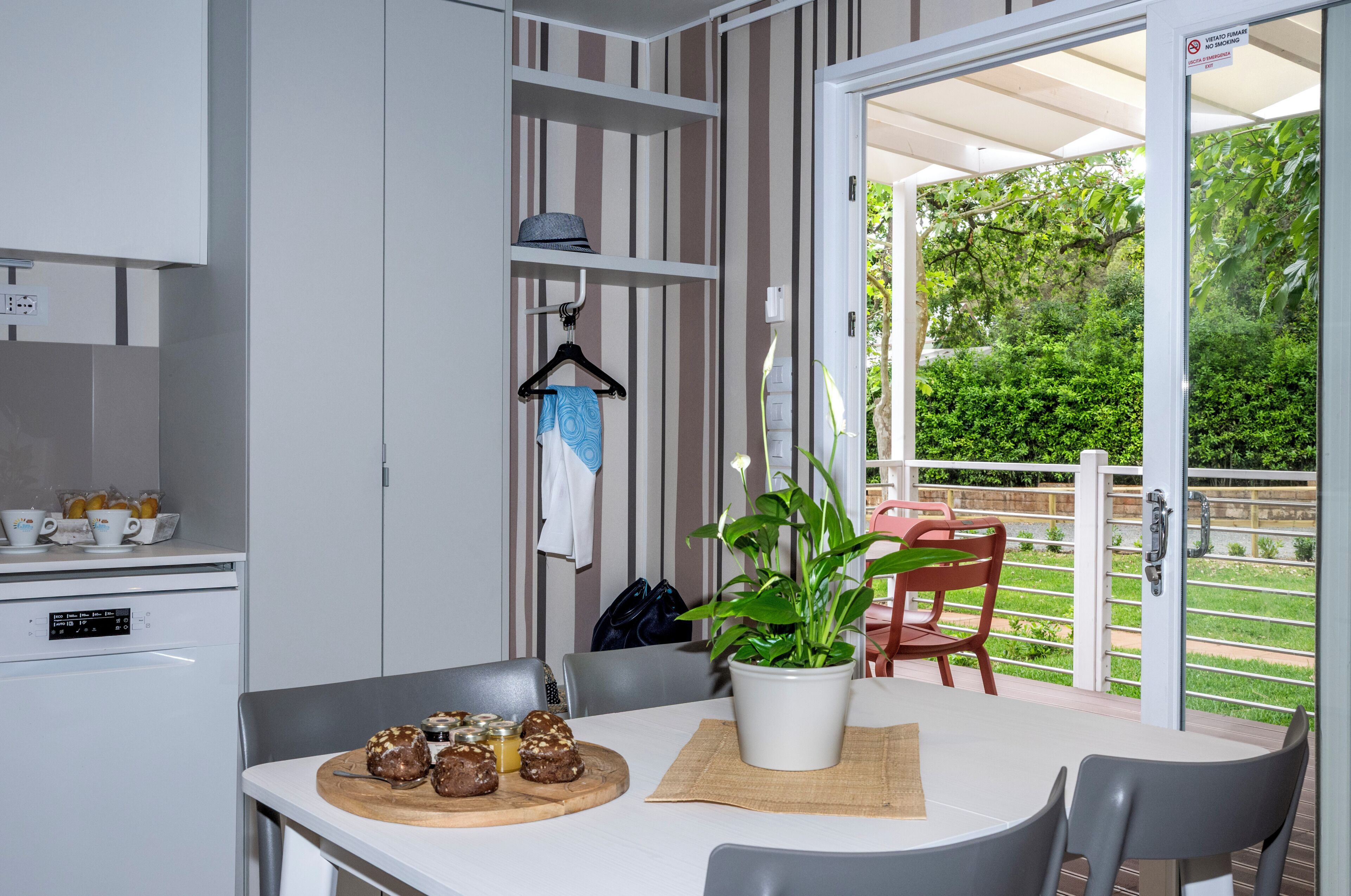 A dining area with a table, chairs, a potted plant, and a view of a garden through a sliding glass door.