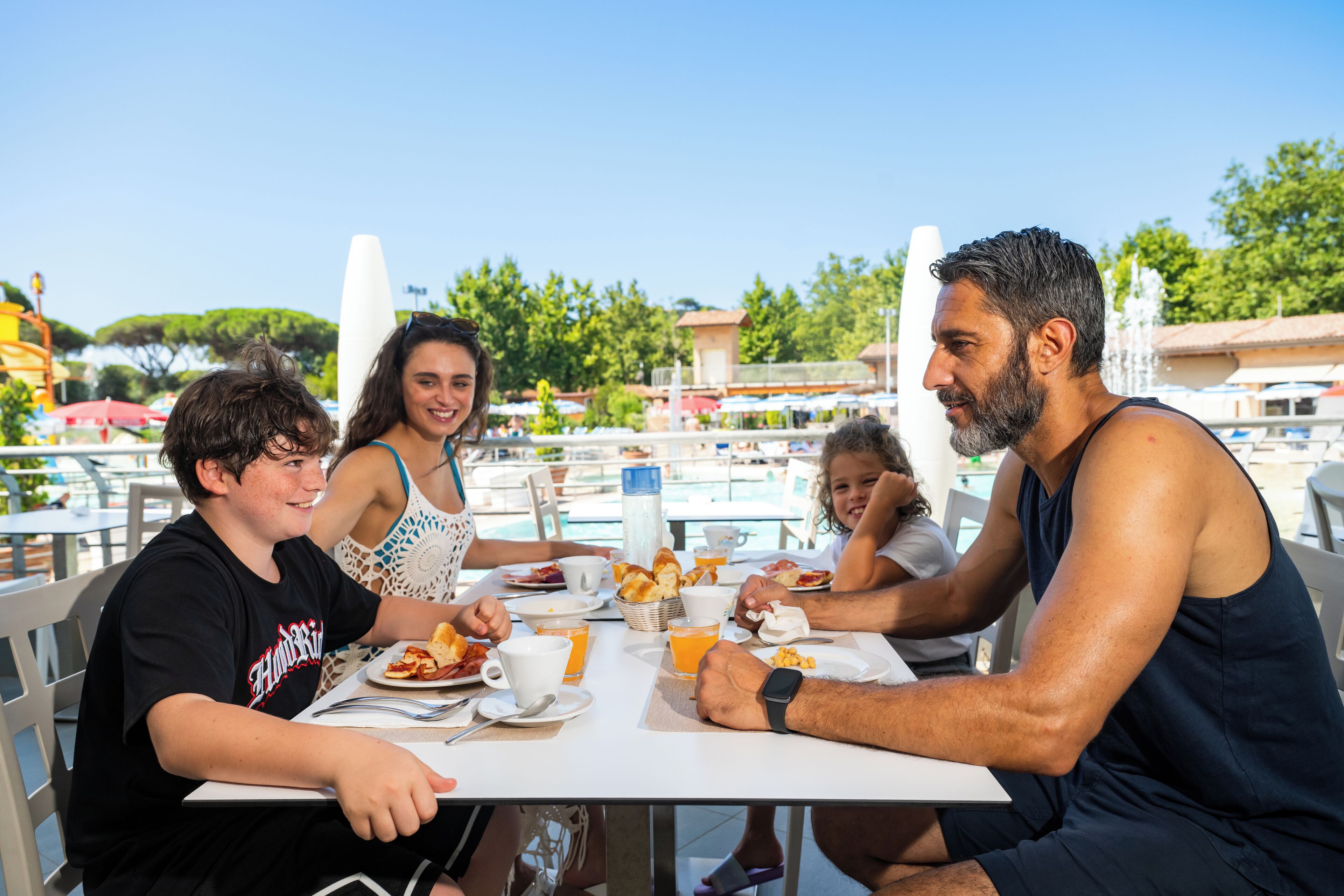 A family dining at an outdoor table with a view of a pool and trees.