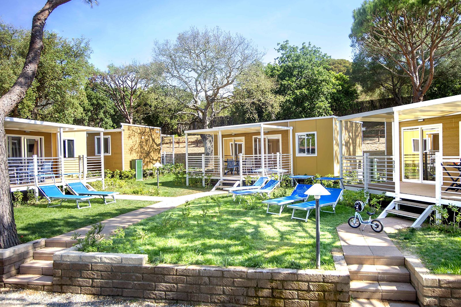 A row of single-story cabins with outdoor seating areas and a small garden.