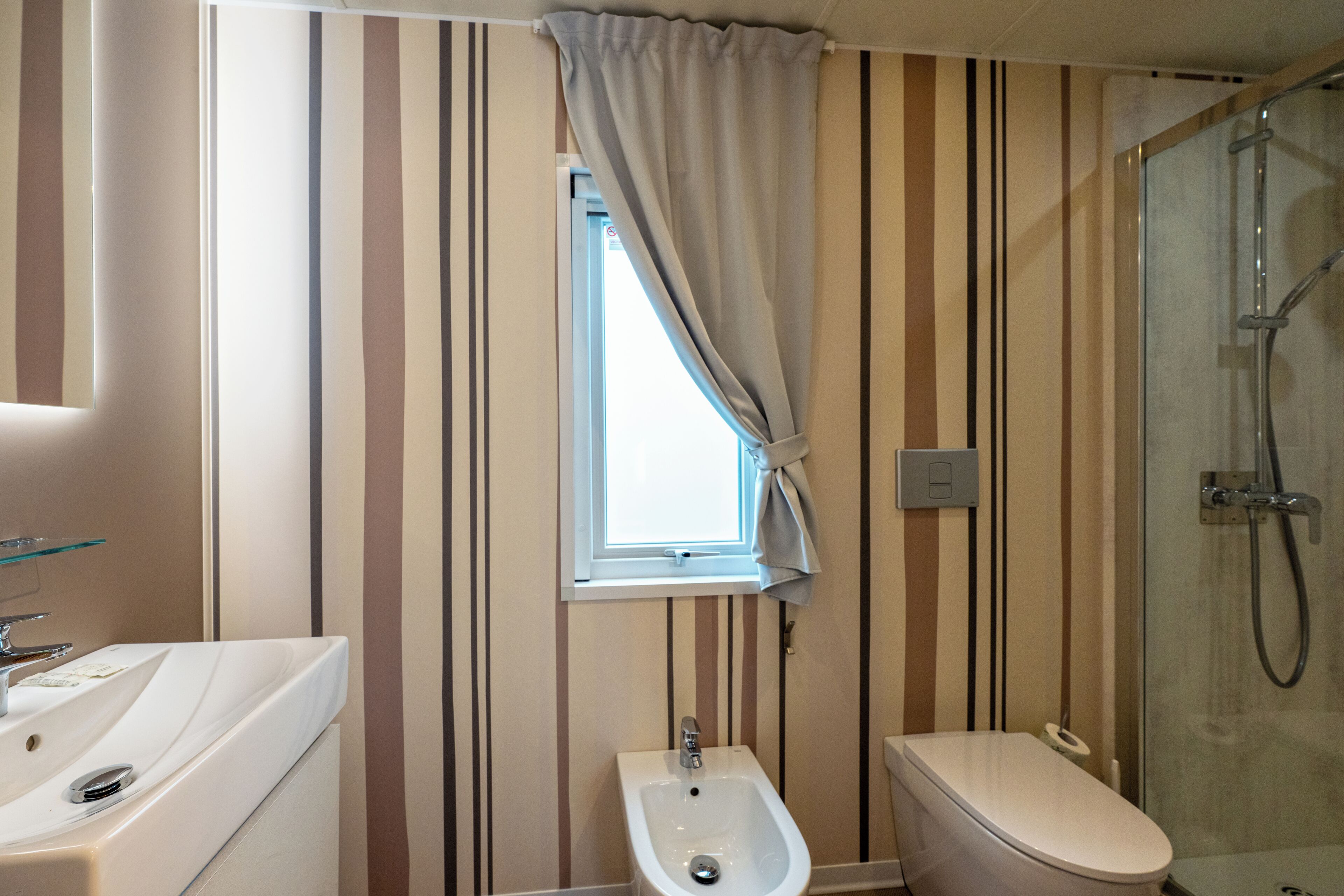 Baño con bidé, inodoro y ventana con cortinas.