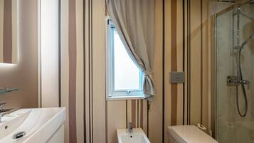 Baño con bidé, inodoro y ventana con cortinas.