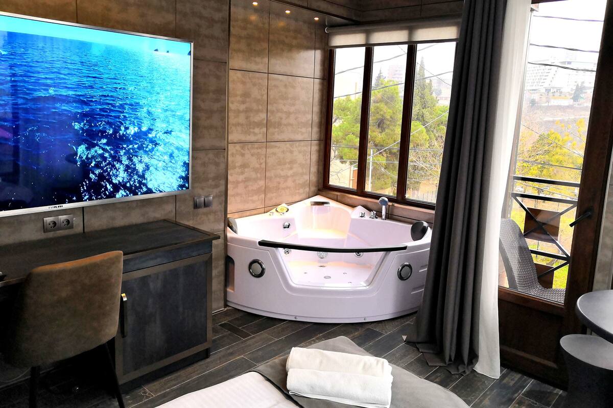 A modern bathroom with a large bathtub, a flat-screen TV, and a view of the outdoors.