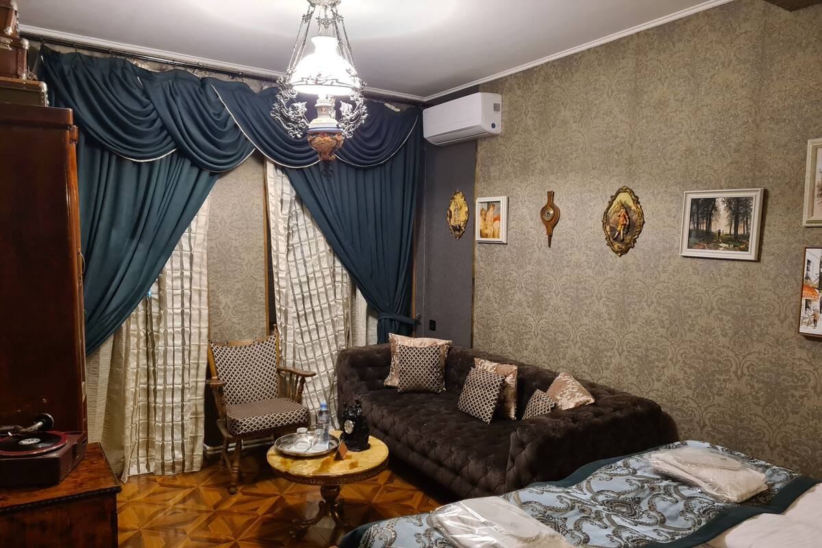 A room with a sofa, a chair, a small round table, a bed, and a ceiling light.