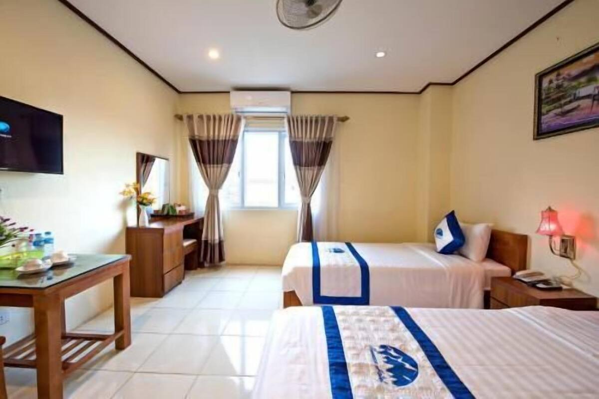 A hotel room with two beds, a desk, a TV, and a window with curtains.