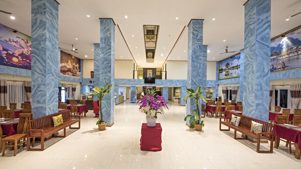 A spacious lobby with marble columns, wooden benches, and tables, featuring a central floral arrangement and artwork on the walls. - Annecy Hotel Vang Vieng (Vang Vieng)