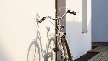 Een fiets leunt tegen een witte muur, met de schaduw van een andere fiets.