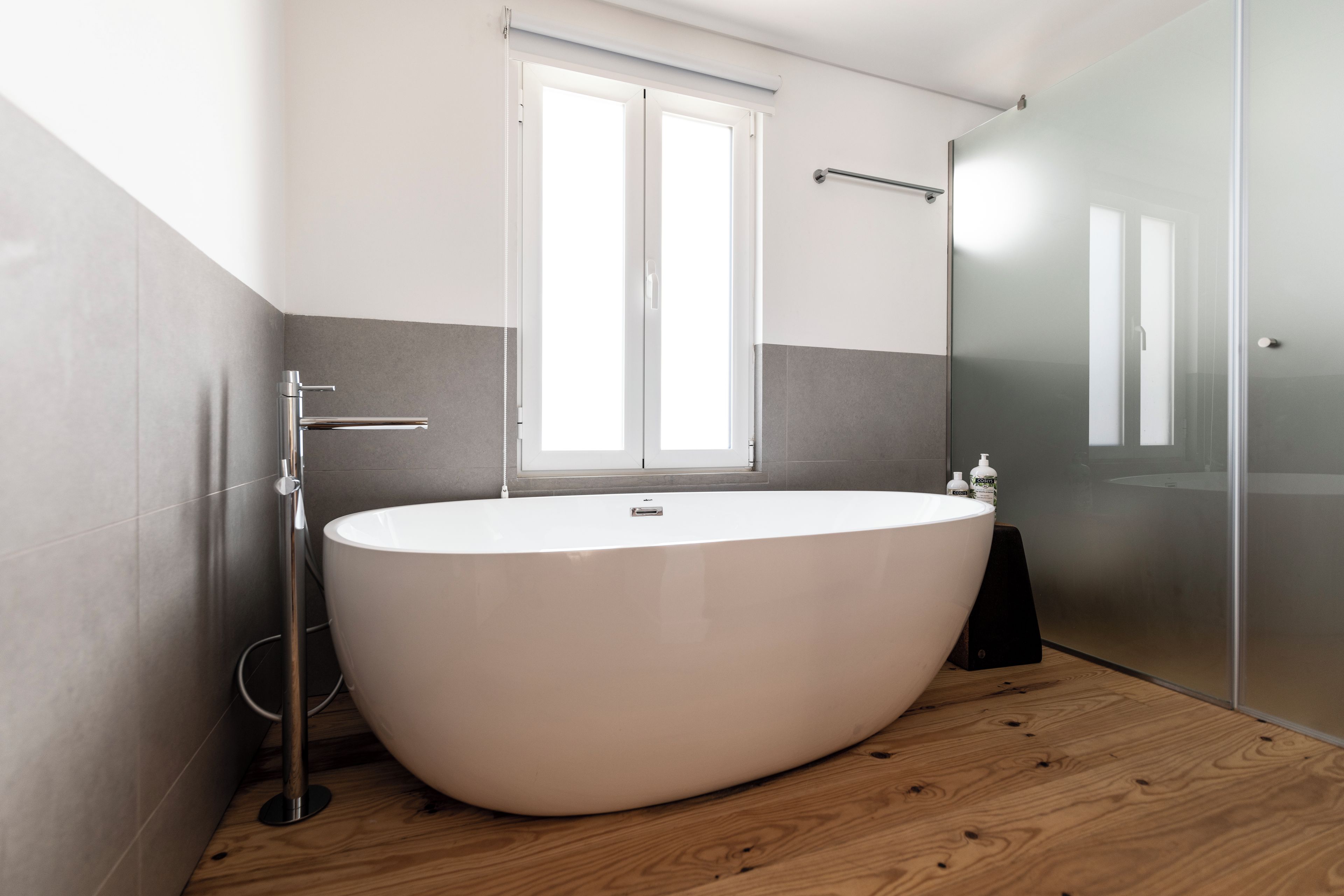 Ein modernes Badezimmer mit einer freistehenden Badewanne, einem Fenster und einer Glasdusche.