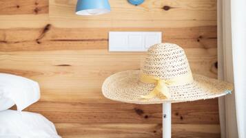 A wooden wall with a blue lamp, a white bedside table with a drawer, and a straw hat on the table.