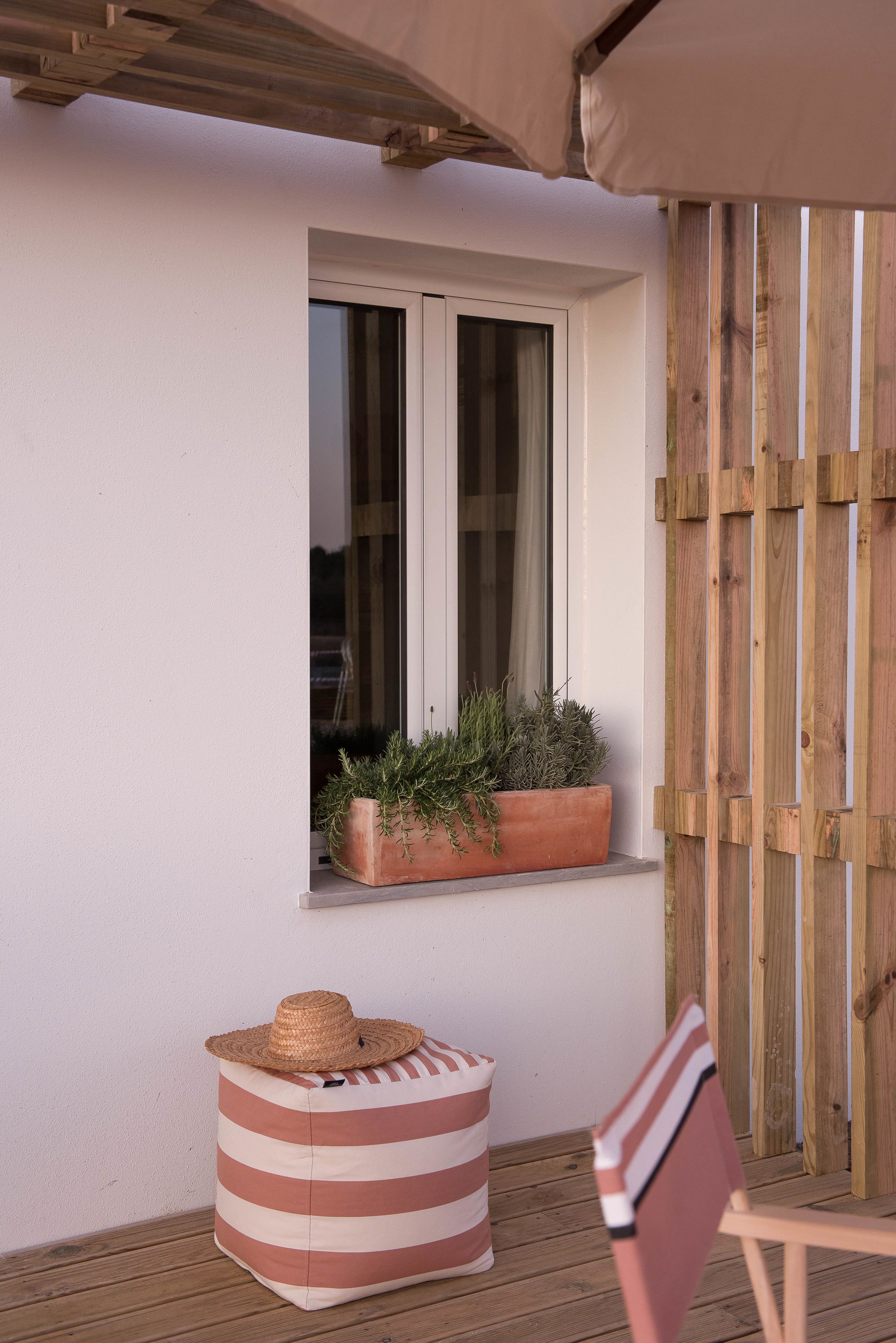 A wooden deck with a window, a potted plant, a striped bean bag, and a straw hat.
