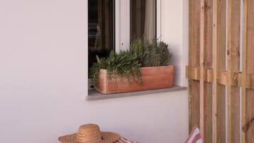 A wooden deck with a window, a potted plant, a striped bean bag, and a straw hat.