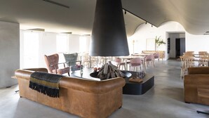 Un salon spacieux avec des canapés en cuir, une cheminée centrale et un plafond haut.