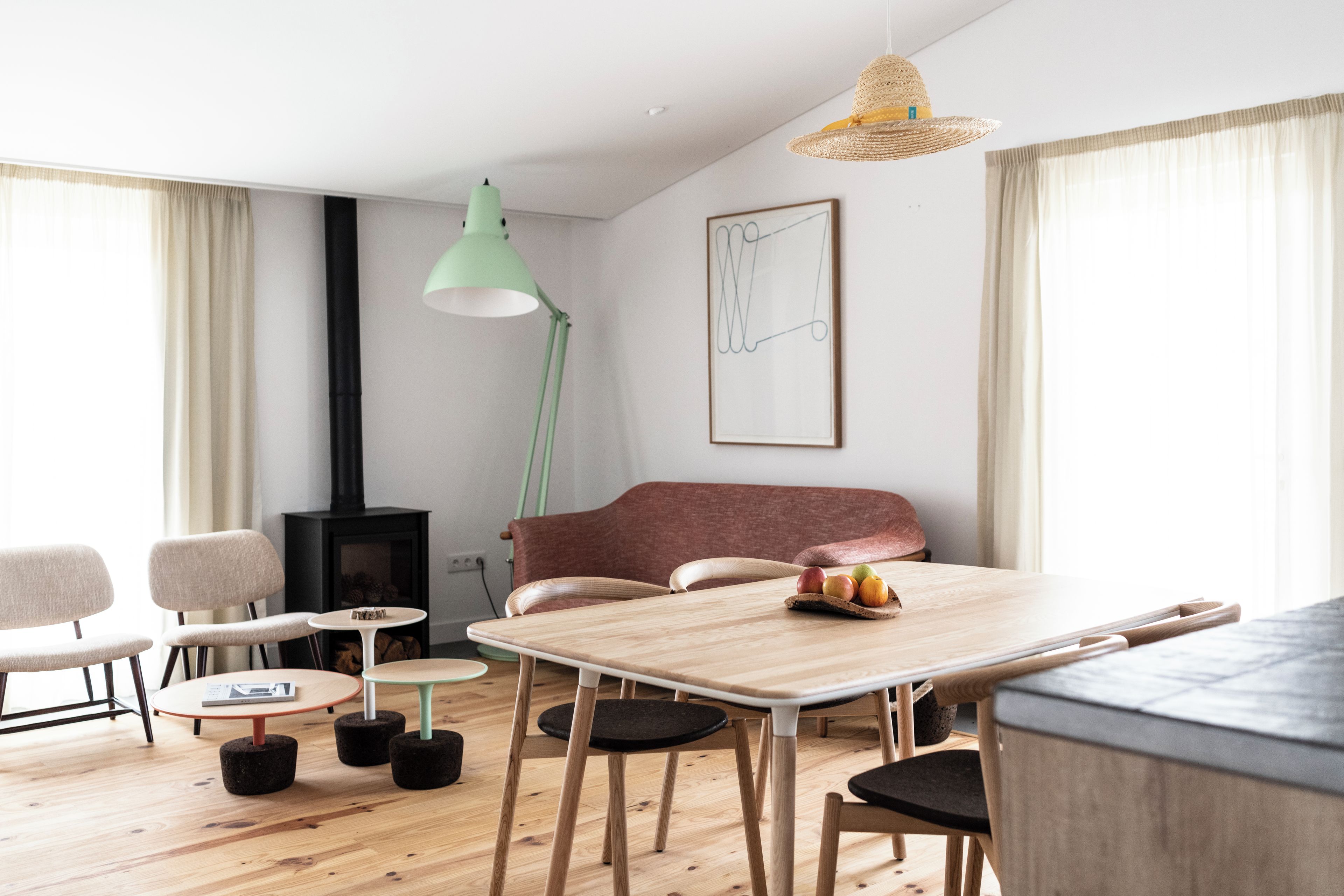 A modern living room with a wooden dining table, chairs, a sofa, a fireplace, and a hanging light fixture.