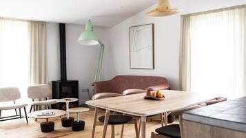 A modern living room with a wooden dining table, chairs, a sofa, a fireplace, and a hanging light fixture.