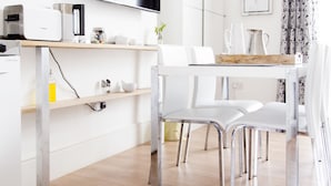 Una cocina moderna con televisión de pantalla plana, electrodomésticos blancos y un comedor con sillas blancas y una mesa de madera.