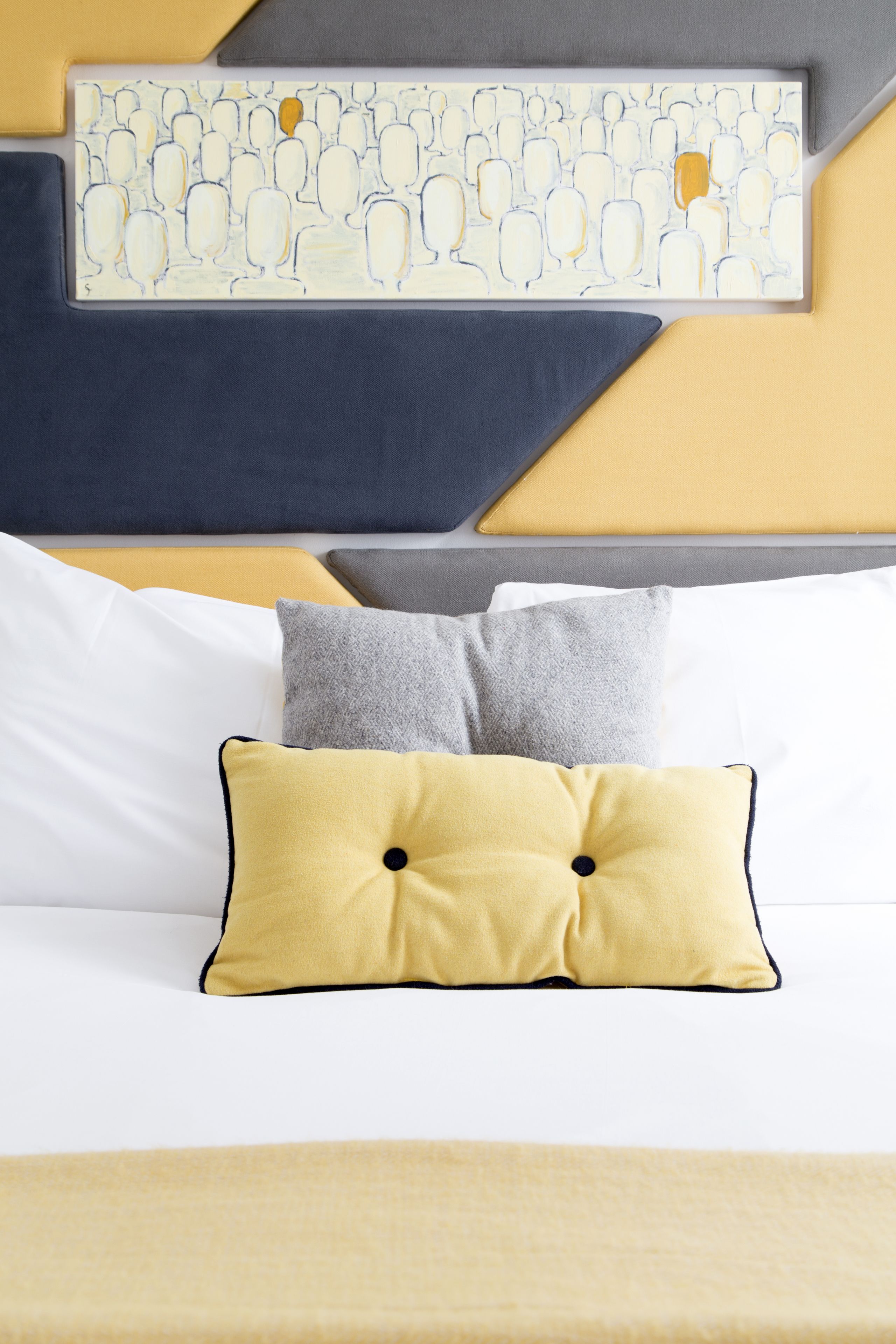 A neatly arranged bed with a yellow pillow, a gray pillow, and a white pillow.