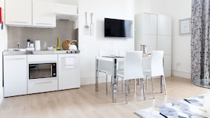 Una cocina moderna con armarios blancos, horno empotrado y comedor con mesa de vidrio y sillas blancas.