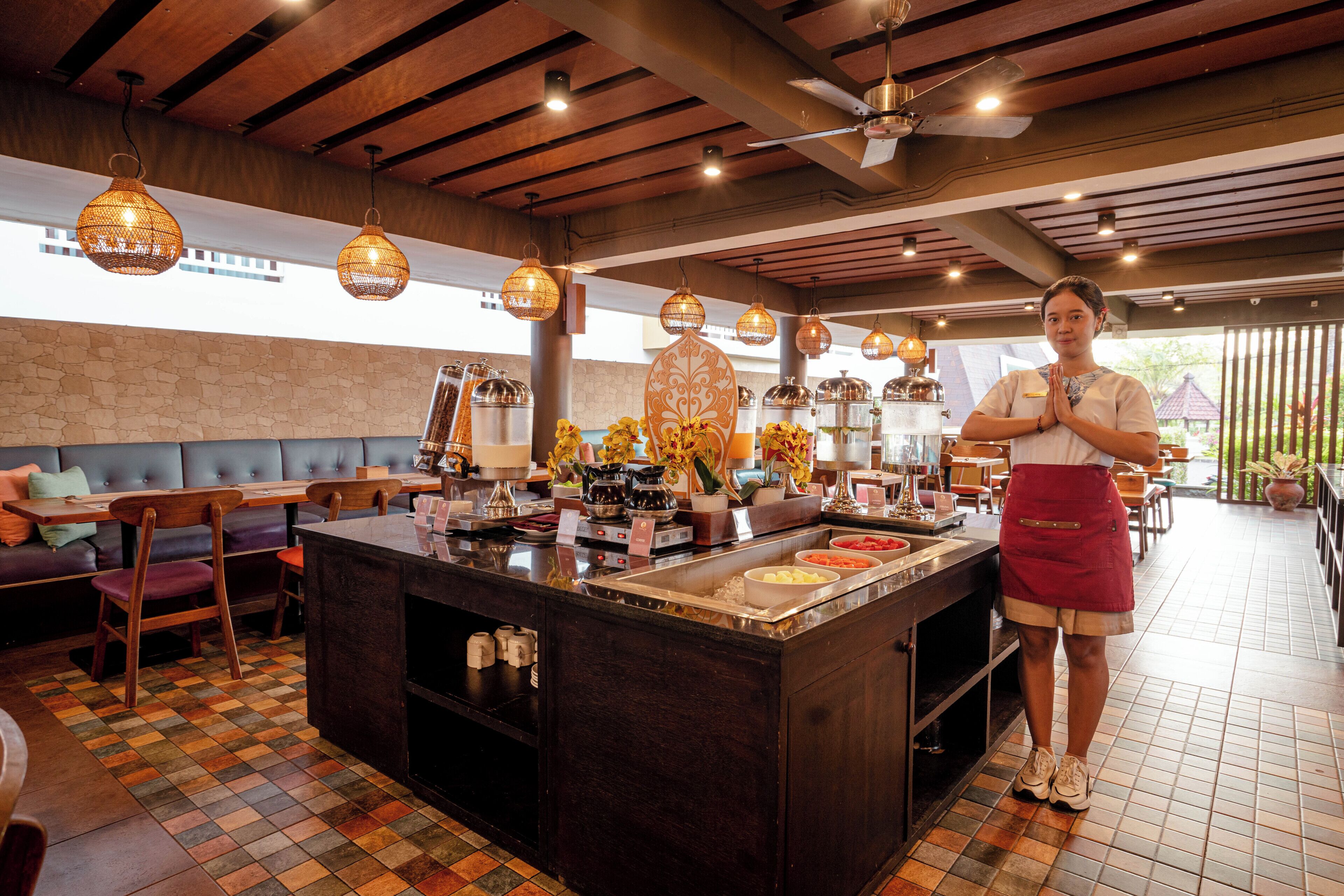 Un restaurante con barra central, mesas y sillas, y una persona de pie cerca de la barra.