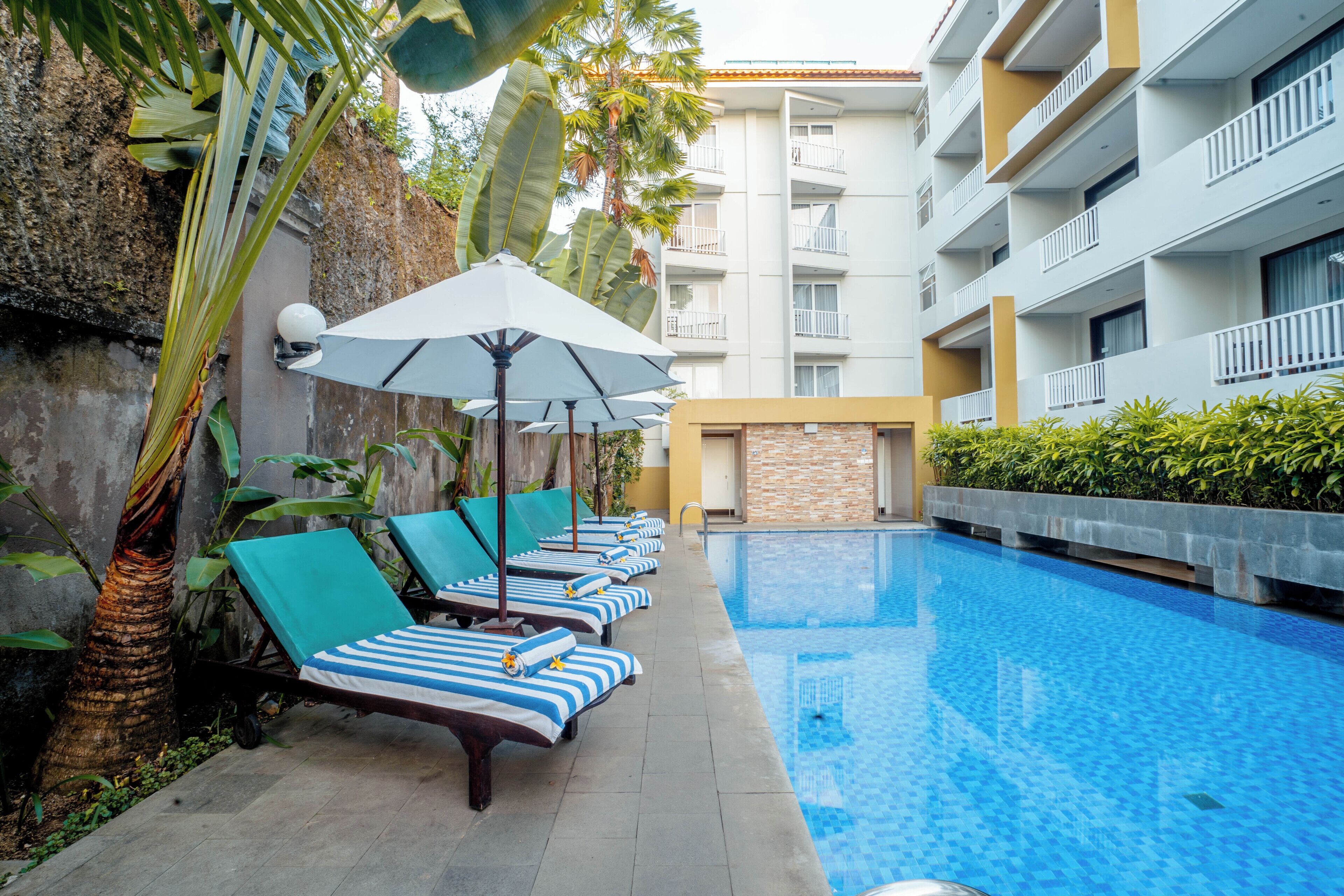 Une piscine entourée d’un bâtiment doté de balcons, avec des chaises longues et des parasols à proximité.