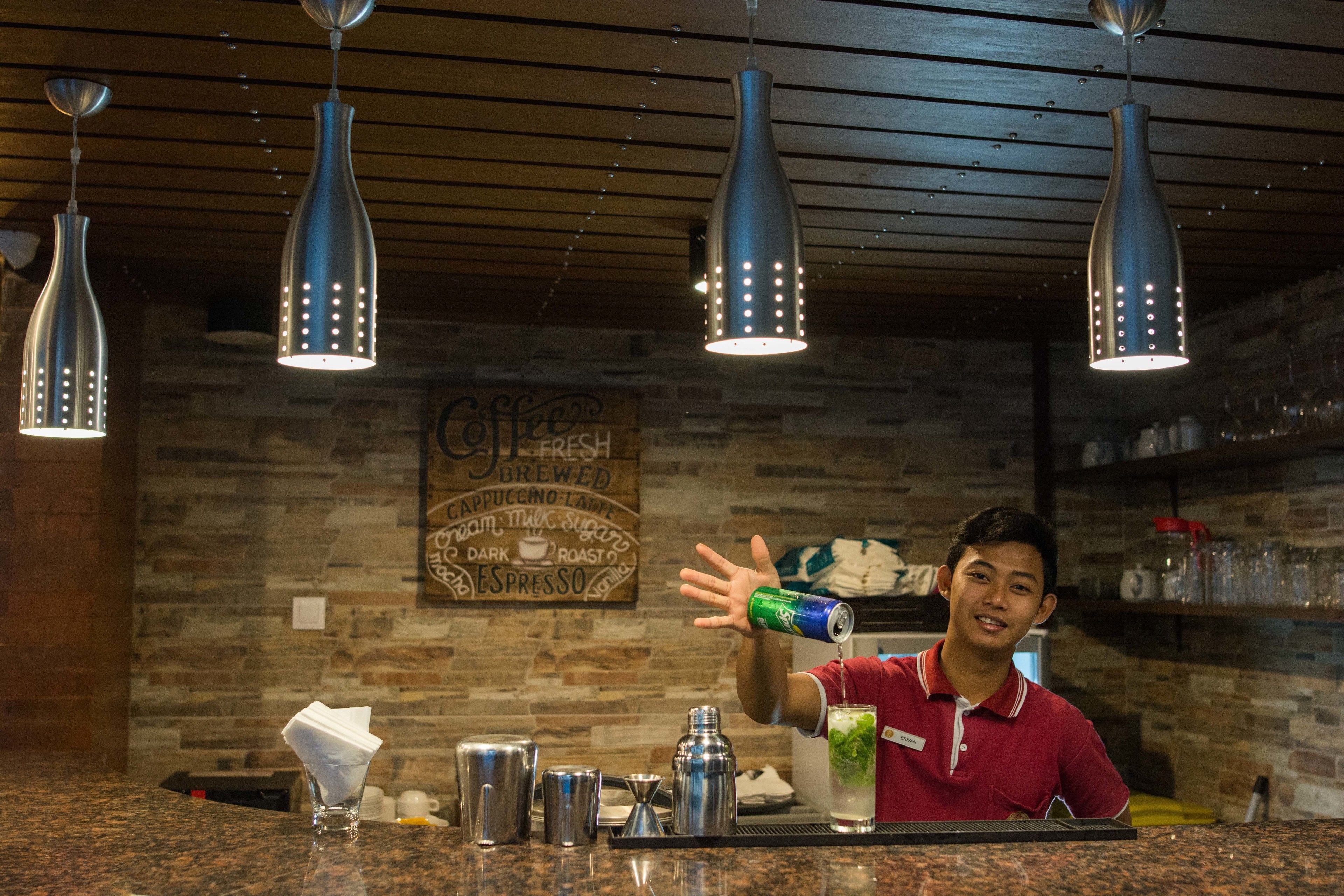 A bar area with hanging pendant lights, a counter with various bar tools, and a menu board in the background.