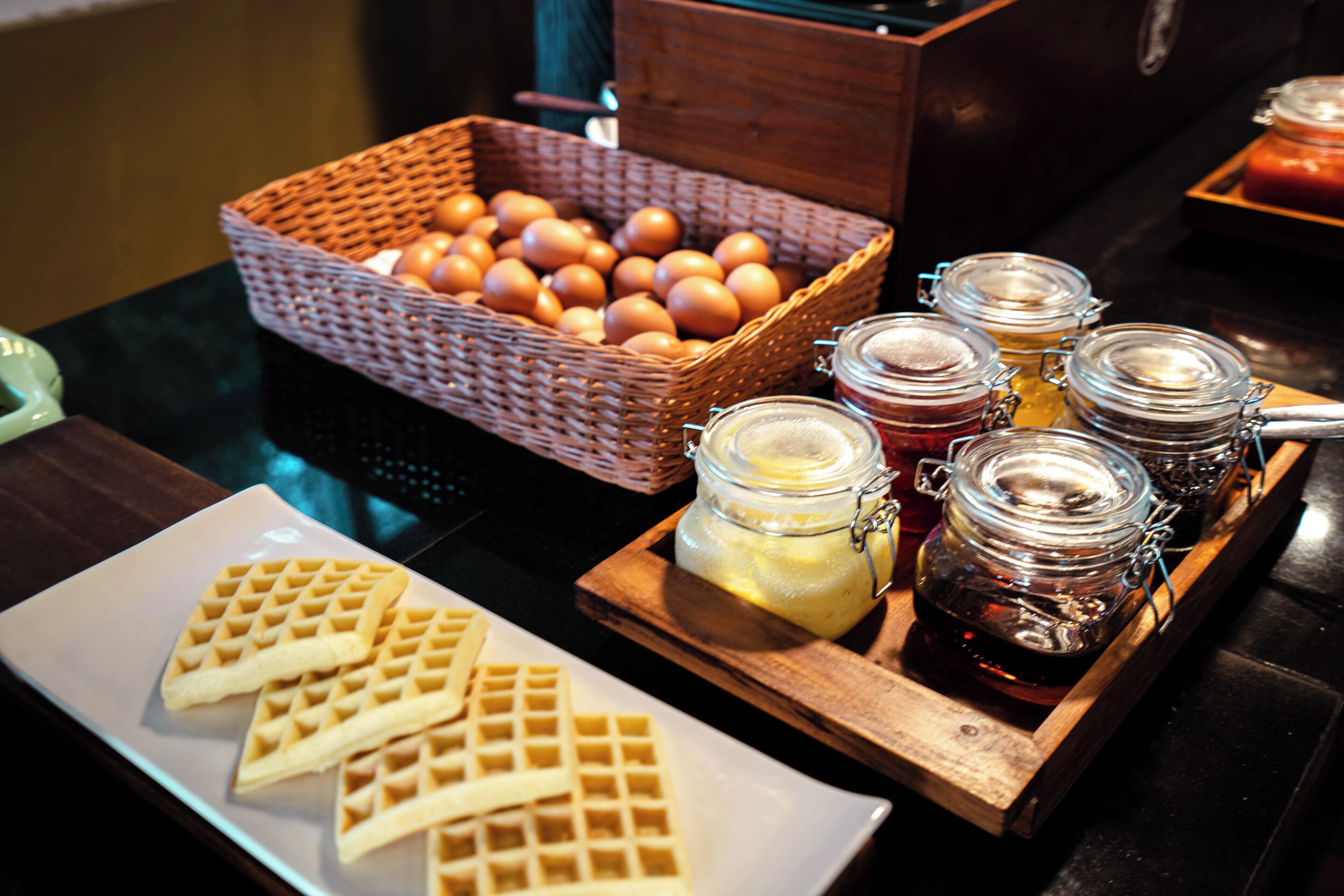Een ontbijtbuffet met wafels, eieren en diverse jamsoorten en beleg.