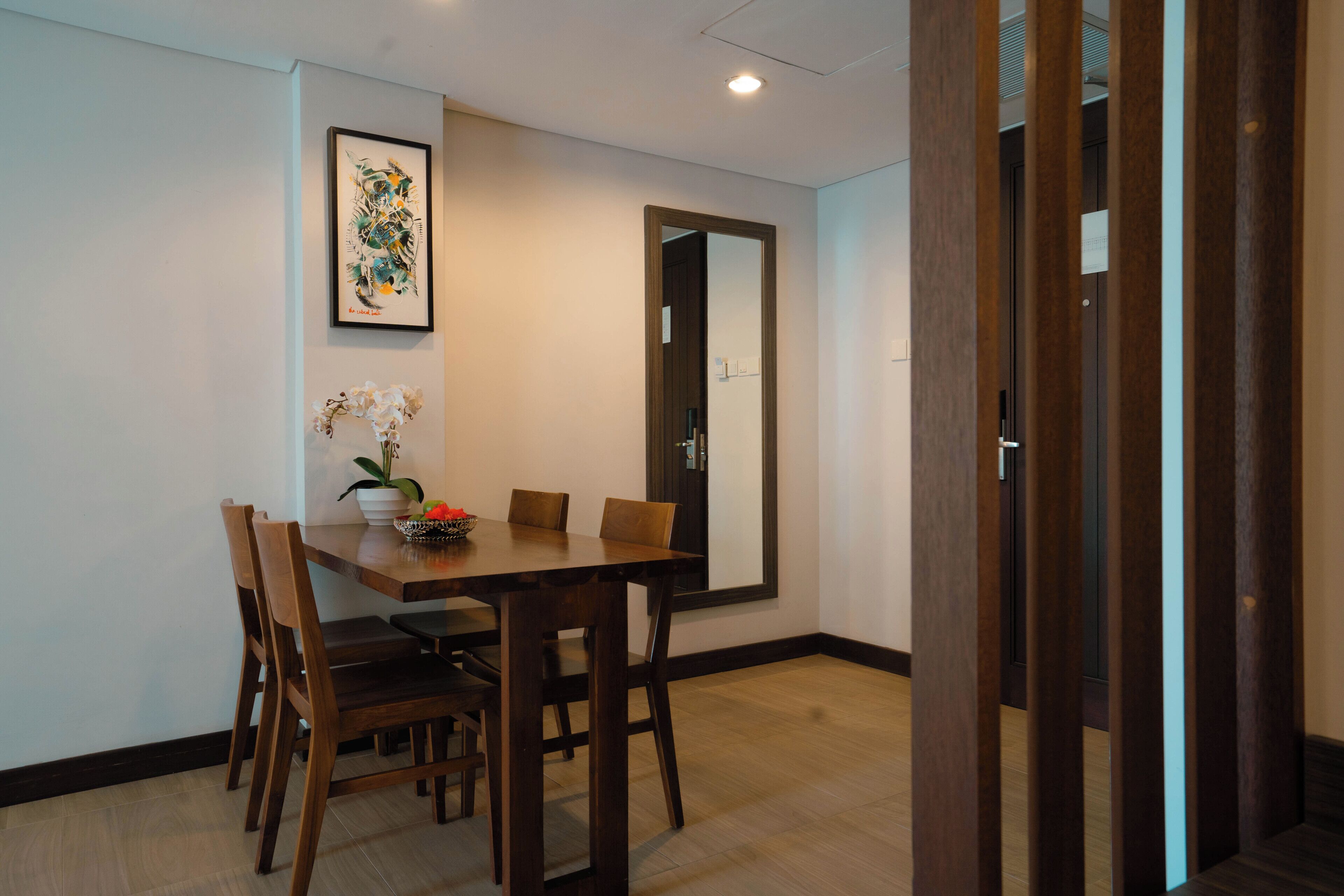 A dining area with a wooden table and chairs, a framed artwork on the wall, and a door in the background.