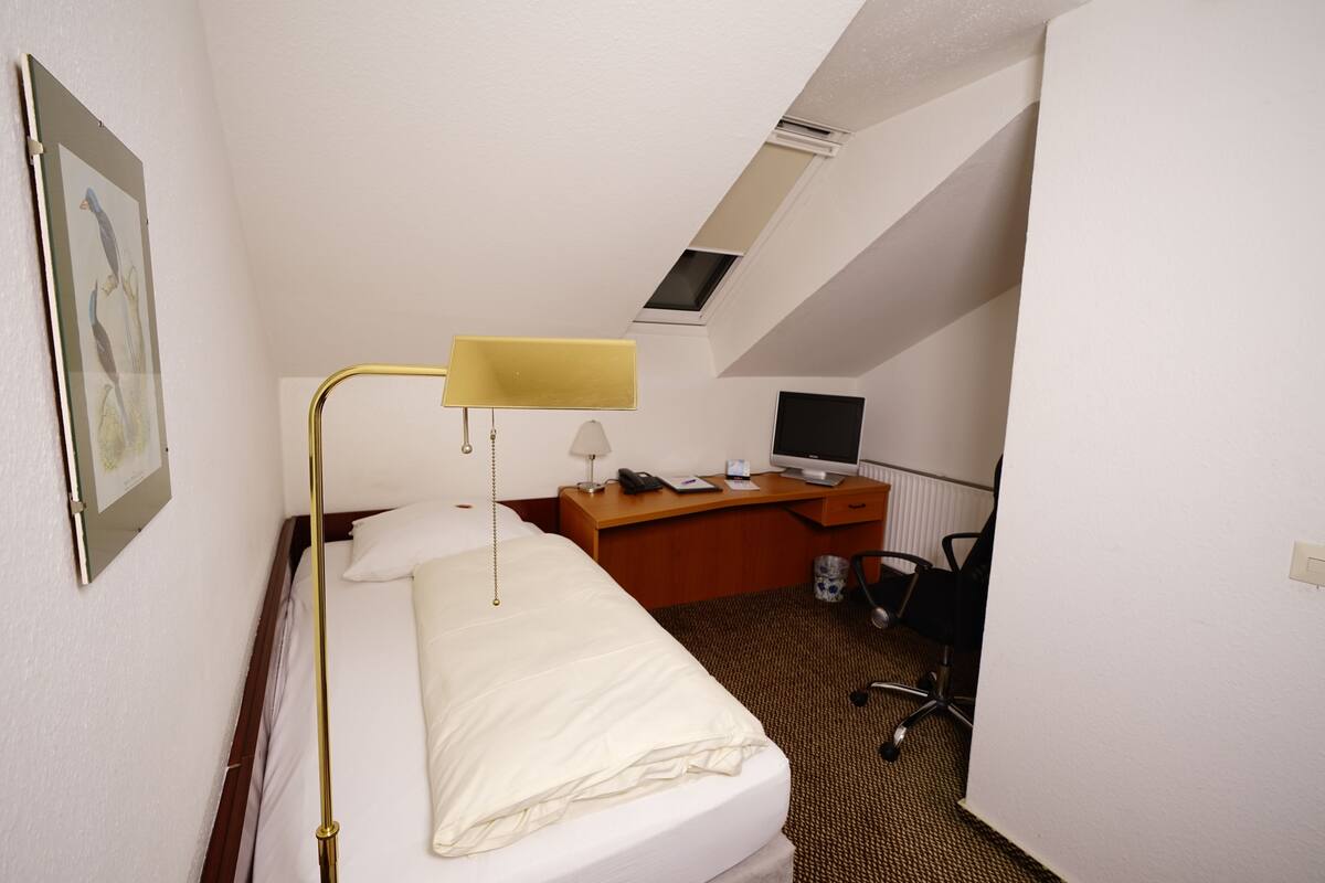 Une chambre d’hôtel avec un lit, un bureau équipé d’un ordinateur, une chaise et une fenêtre donnant sur le ciel.