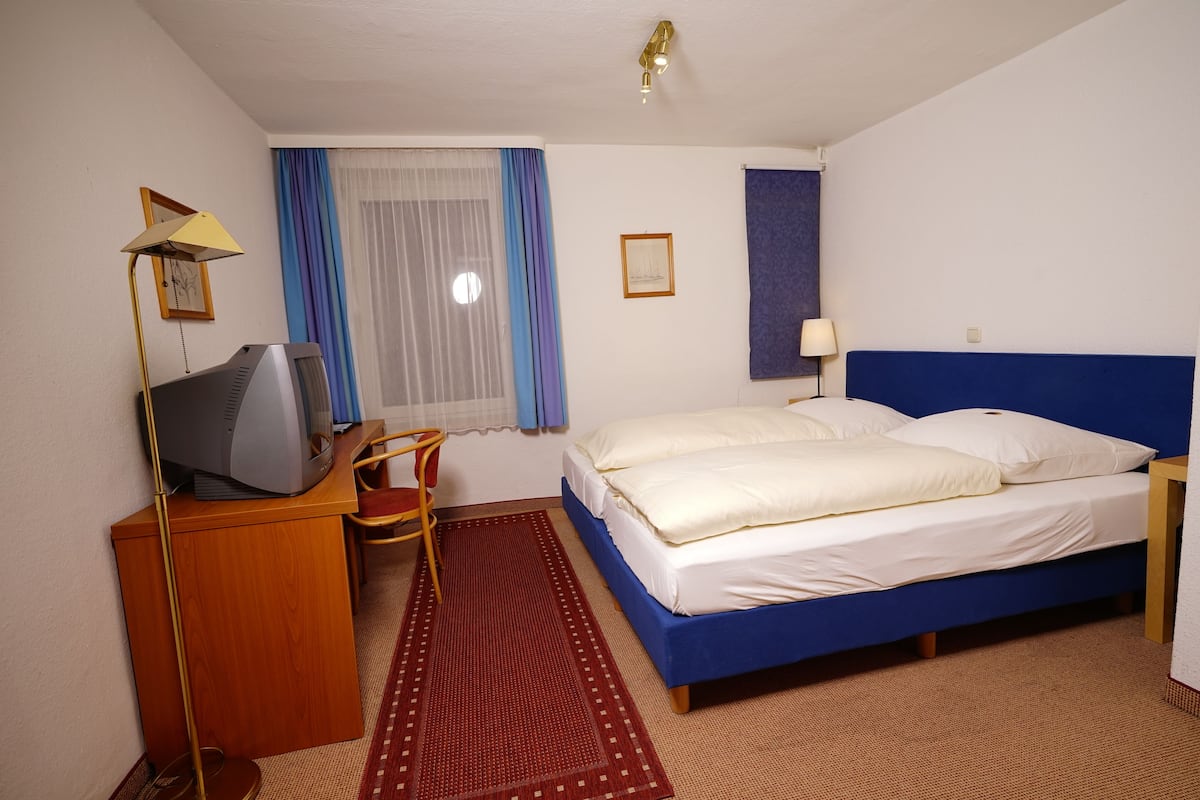 Une chambre d’hôtel comprenant un lit, un bureau avec une télévision, une chaise, une fenêtre avec des rideaux et une lampe fixée au mur.