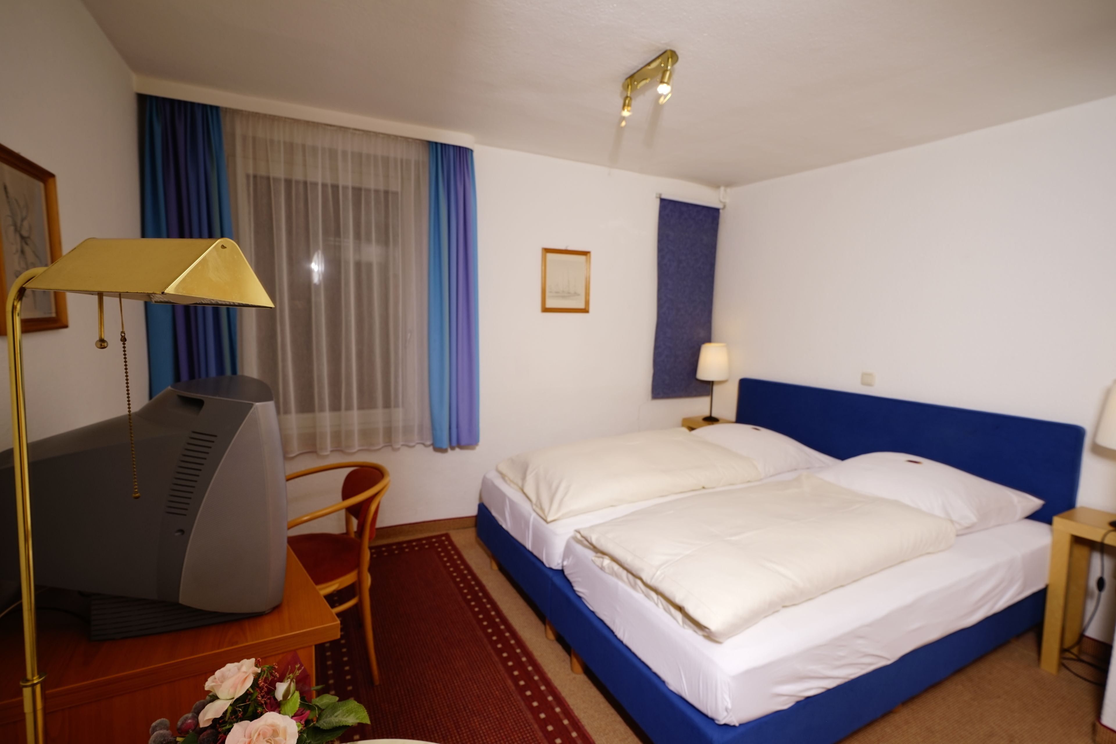 Een hotelkamer met een bed, een bureau met een computer, een stoel, een bureaulamp en een raam met gordijnen.