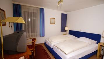 Een hotelkamer met een bed, een bureau met een computer, een stoel, een bureaulamp en een raam met gordijnen.