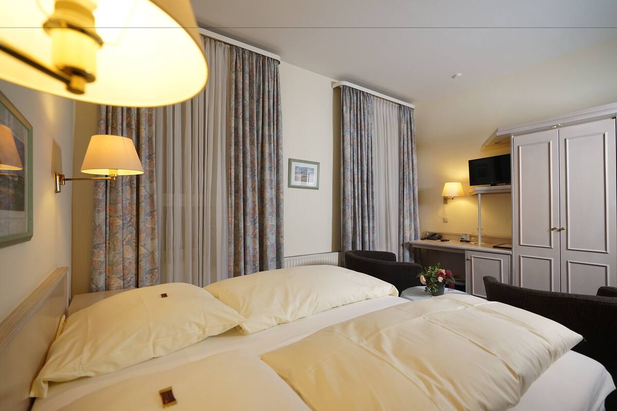 Une chambre d’hôtel avec un grand lit, deux tables de chevet, un bureau avec une chaise, une télévision et une armoire.