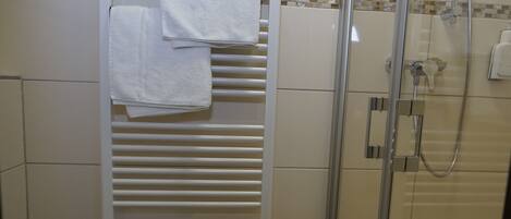 A bathroom with a glass-enclosed shower, a white towel rack with towels, and a toilet.