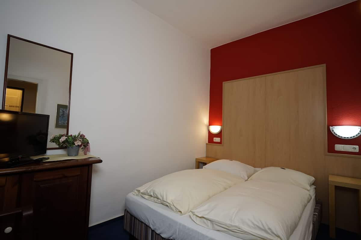 Une chambre d’hôtel équipée d’un lit, d’une télévision, d’une table de chevet, d’un miroir et d’une lampe fixée au mur.