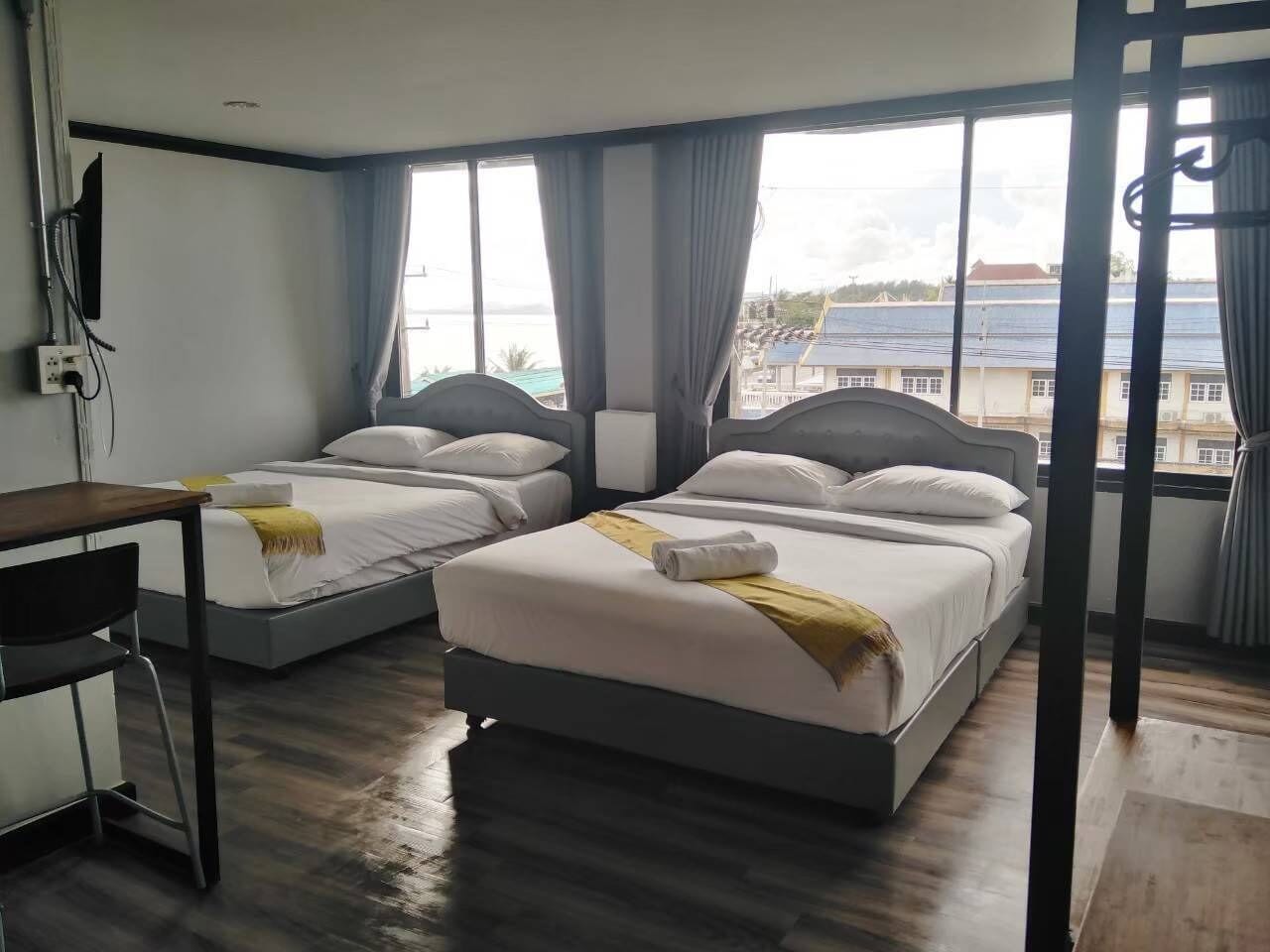 A hotel room with two beds, a desk, and a view of the sea.