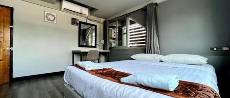 Habitación de hotel con una cama grande, un escritorio, una silla, un espejo y una ventana con cortinas.