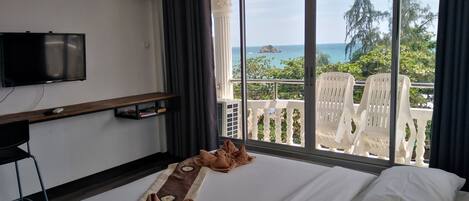 A hotel room with a bed, a TV, a desk with a computer, and a balcony with a view of the sea.