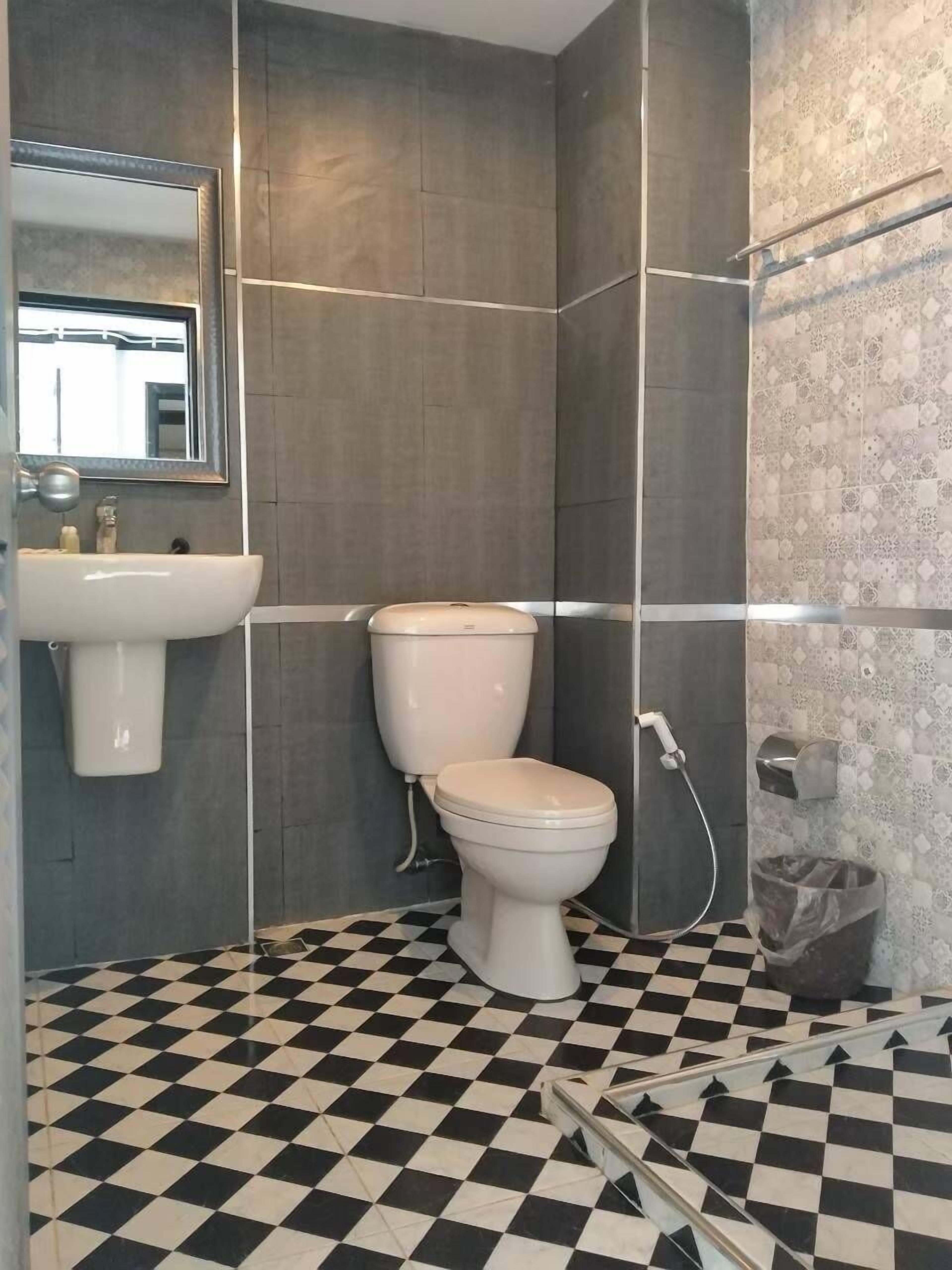 A bathroom with a white sink, toilet, and shower. The floor has a black and white checkered pattern.