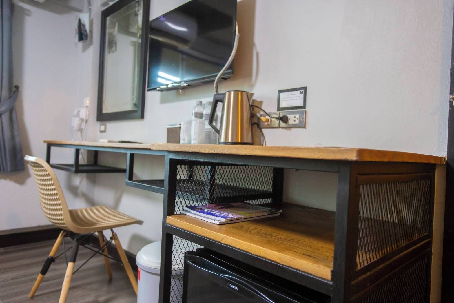 A compact room with a wooden desk, a chair, a TV mounted on the wall, and a trash bin.
