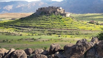 Une forteresse historique, perchée sur une colline verdoyante, avec des champs en terrasses et des montagnes en arrière-plan.