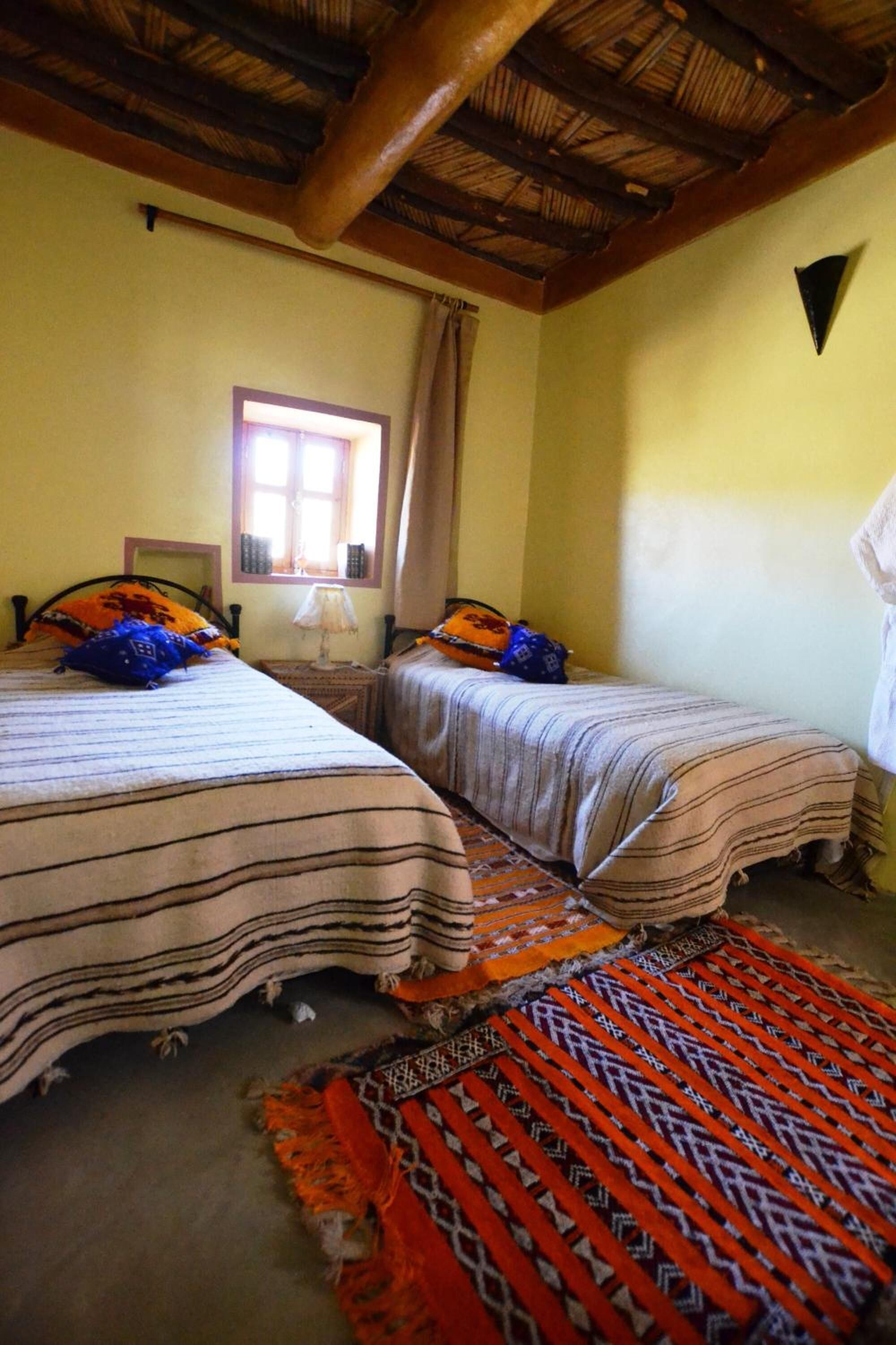 A room with two beds, a window, and a wooden ceiling.