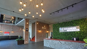 A reception area with a green wall, a reception desk, and a staircase leading to an upper level. - Eco Garden Residences (Kandal Stueng)