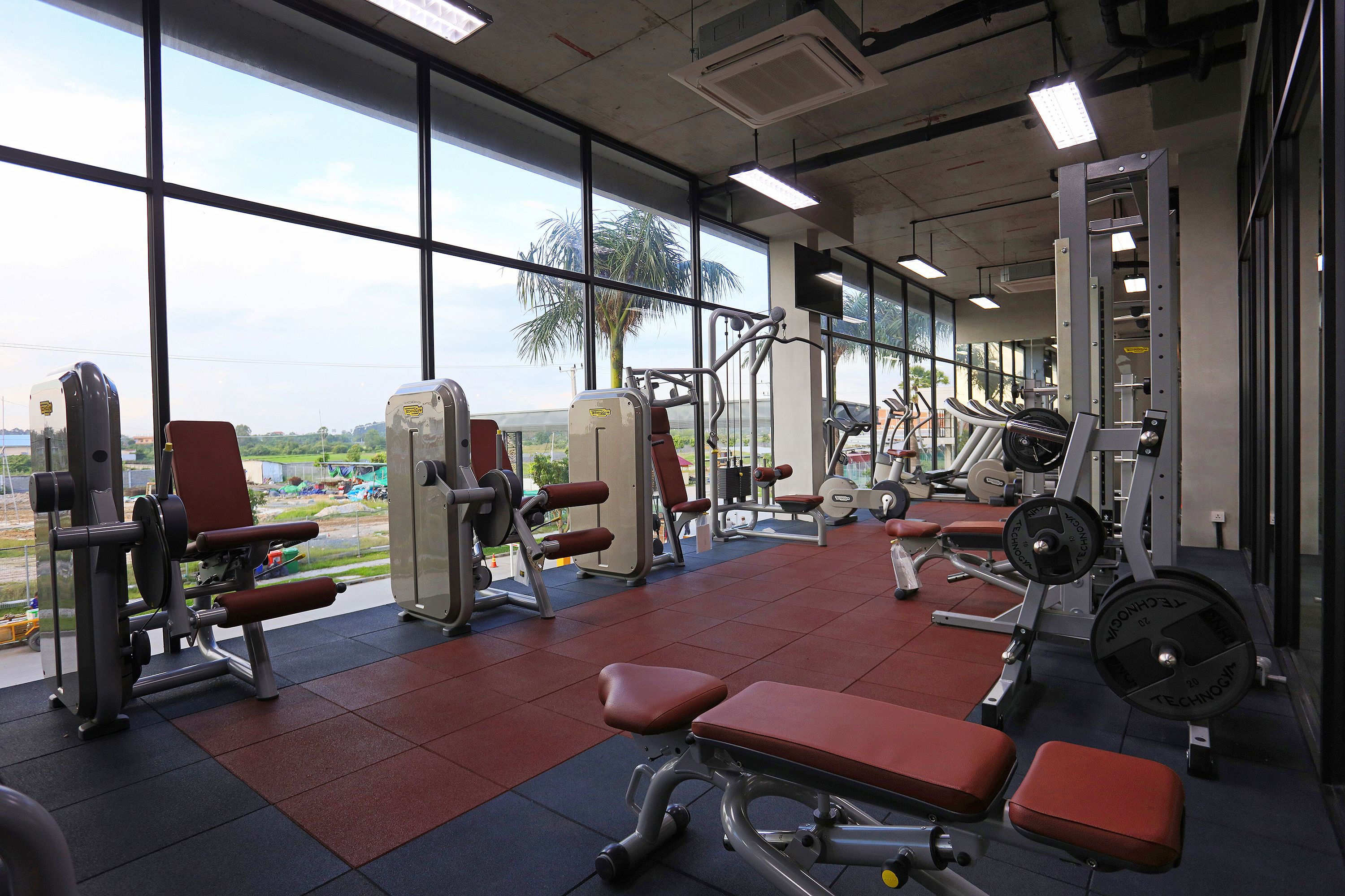 A gym with various exercise equipment, large windows, and a view of the outdoors.