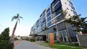 A modern building with a glass facade, a covered entrance, and a landscaped area with trees and a pathway. - Eco Garden Residences (Kandal Stueng)