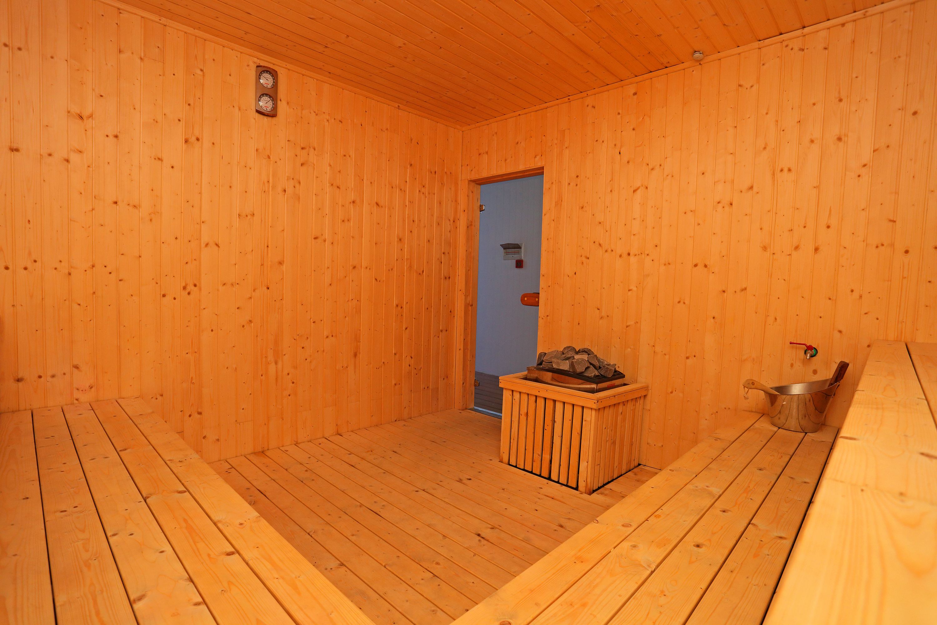 A sauna room with wooden walls and floor, a door, a bench, and a metal container.