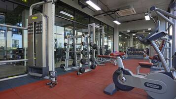 A gym with various exercise equipment, large windows, and a red floor.
