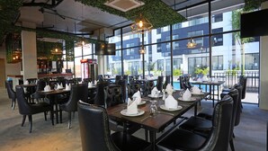 A restaurant with tables set for dining, large windows, and indoor plants. - Eco Garden Residences (Kandal Stueng)