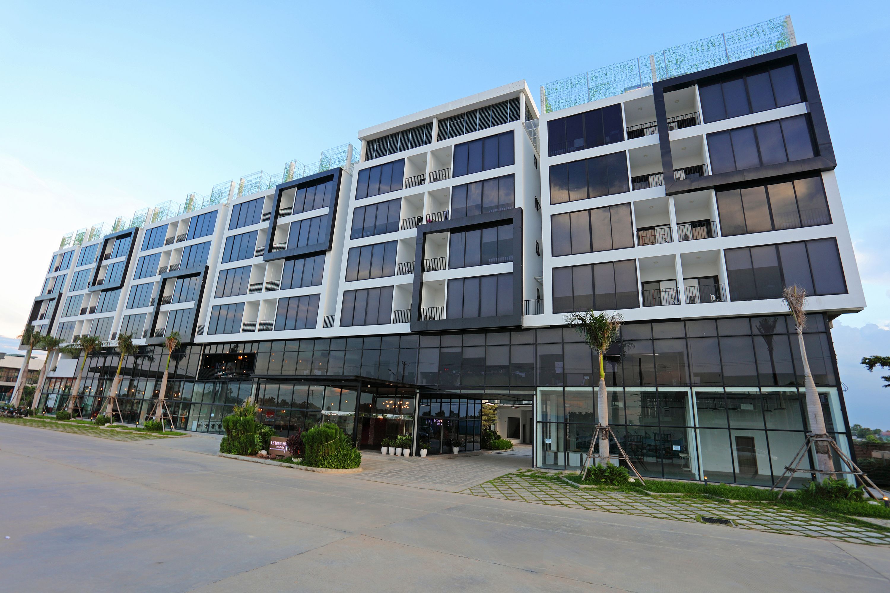 A modern multi-story hotel with a glass facade, multiple balconies, and a landscaped entrance area.