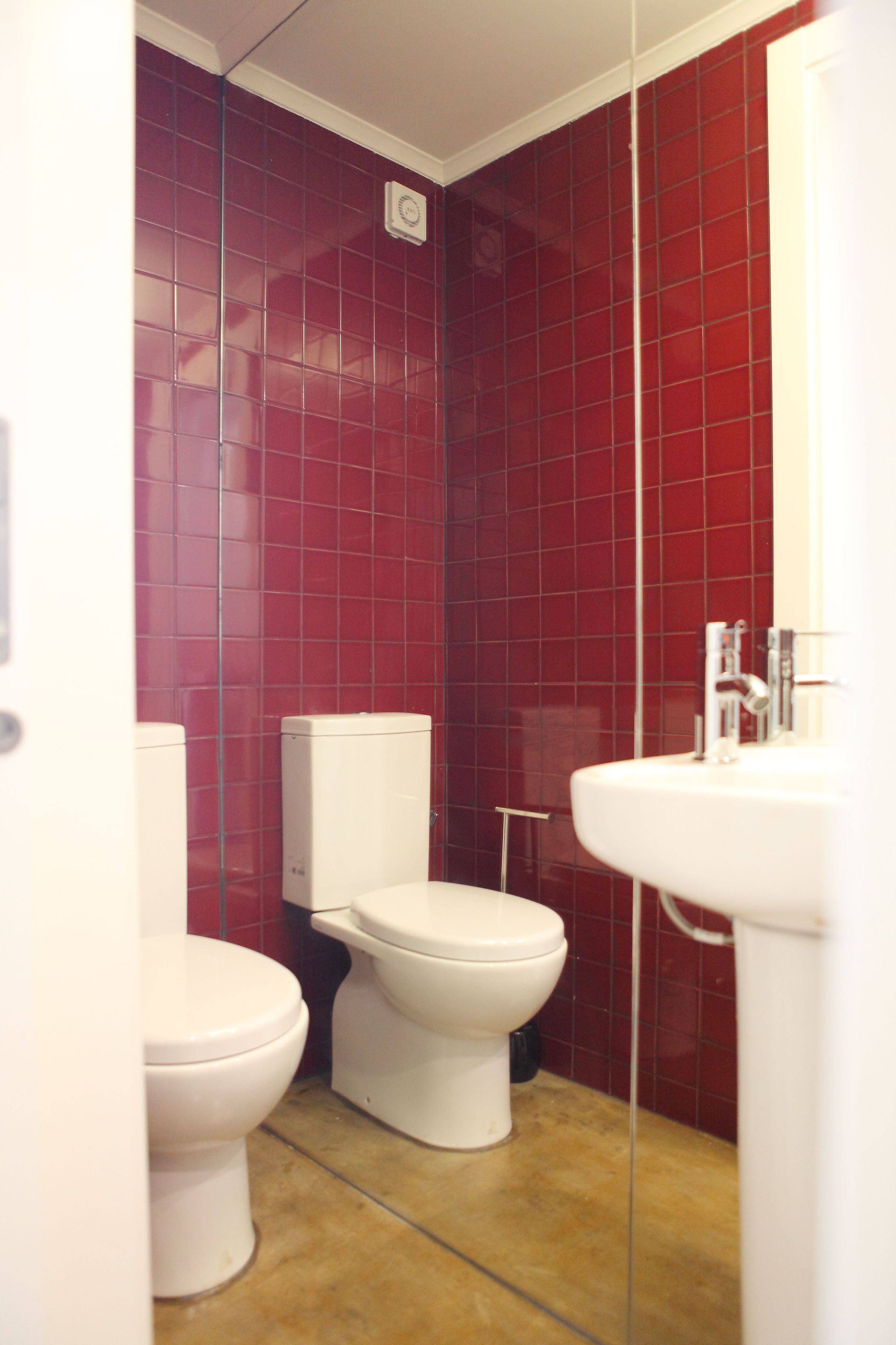 A bathroom with two toilets, a sink, and red tiled walls.